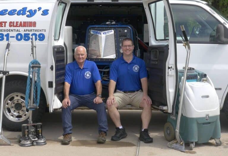 Two carpet cleaners sitting in the back of their van with their equipment