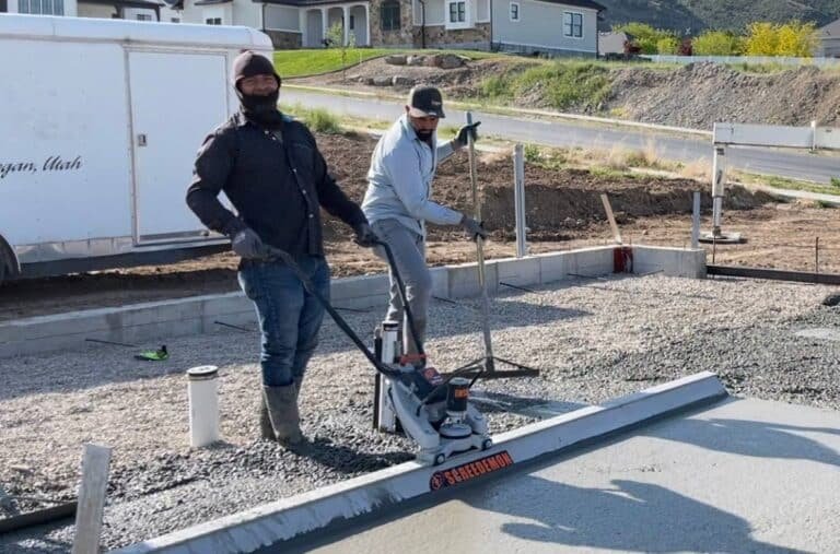 Two concrete contractors finishing a driveway at a house in Logan, Utah