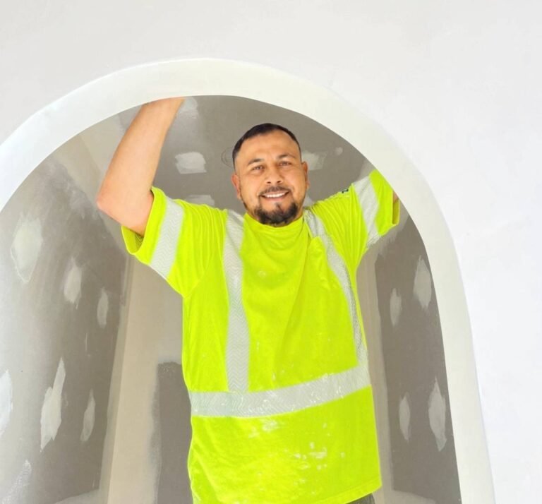 Drywall contractor smiling under a finished plaster archway he just built